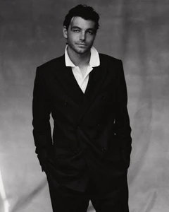 Portrait of Taylor Fritz wearing a dark double-breasted suit and white collared shirt against a textured grey backdrop.