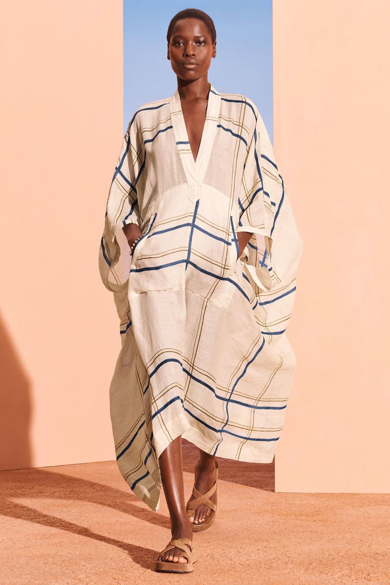 Fashionable woman in a plaid tunic dress and platform sandals confidently poses against a vibrant orange and blue color-block background.