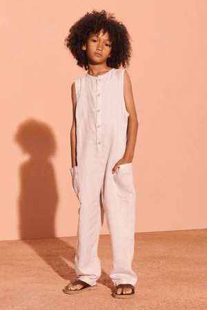 Child model wearing a light pink linen jumpsuit standing against a warm peach studio background for Zara SRPLS Linen 2025.