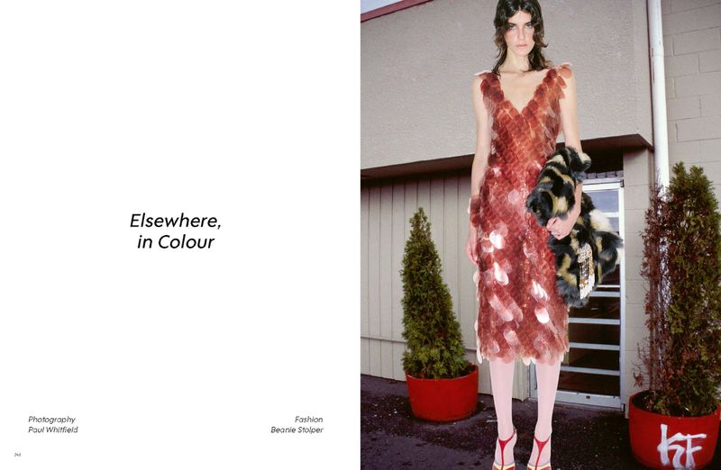 Model in a red sequined dress standing outdoors holding a patterned bag between potted trees for Heroine Magazine