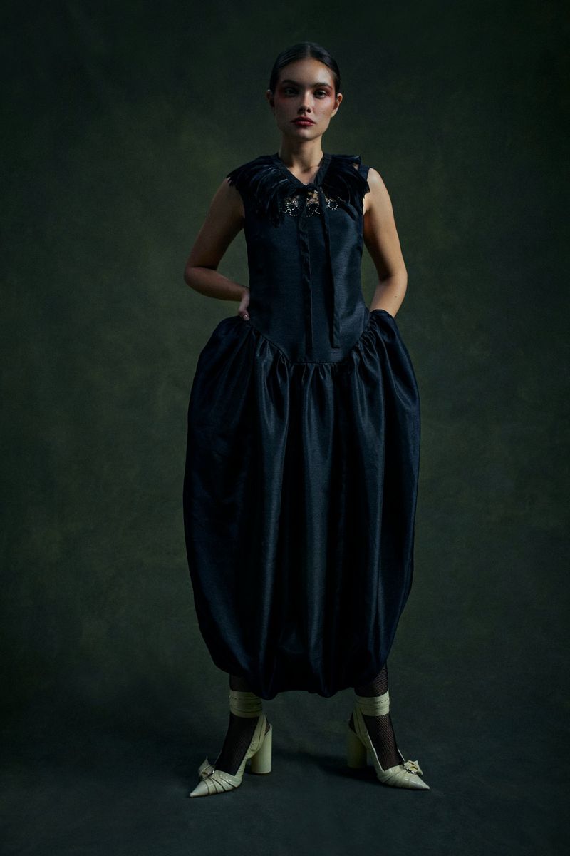 Model wearing a dark ruched dress and cream heels against a dark mottled background for Revista 192 Latitud