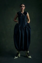 Model wearing a dark ruched dress and cream heels against a dark mottled background for Revista 192 Latitud