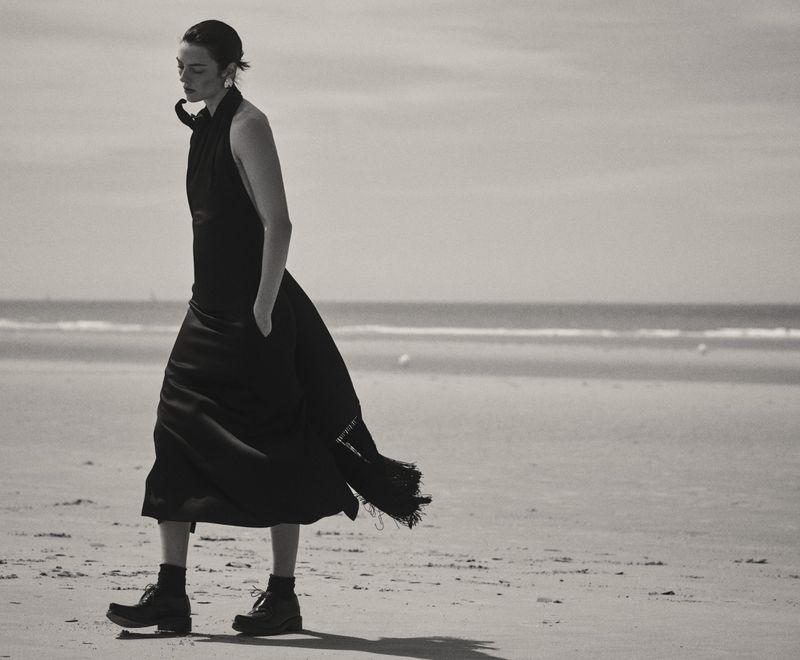 Model Beauïse Genç walking along a sandy beach wearing a dark halter dress and lace-up boots captured by Gregory Harris for Elle France.