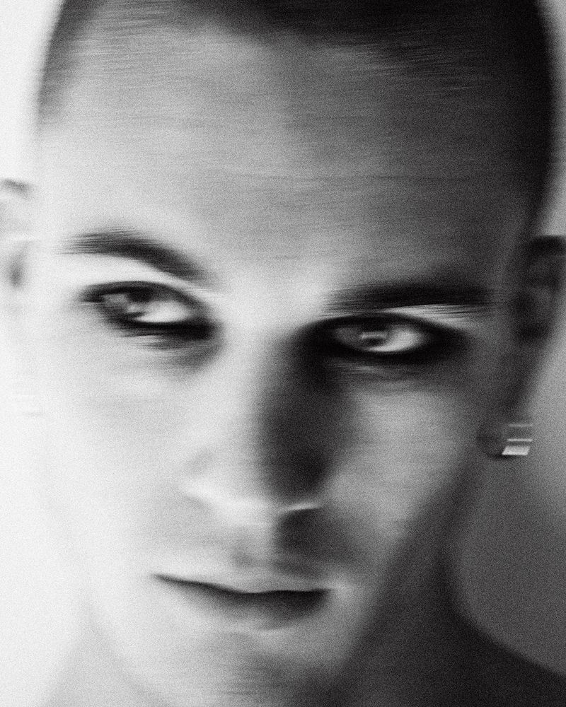 Close-up black and white portrait of a man with dark eye makeup and a motion blur effect