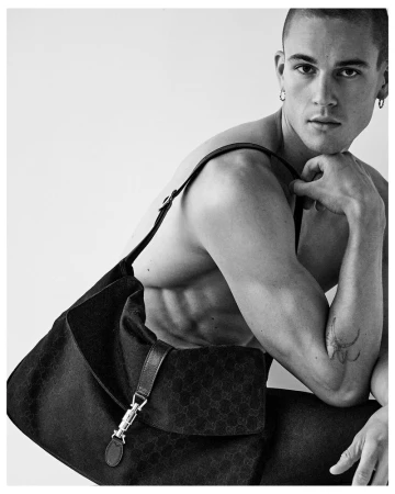Model Samuel Watson wearing a black shoulder bag in a black and white editorial portrait against a plain background