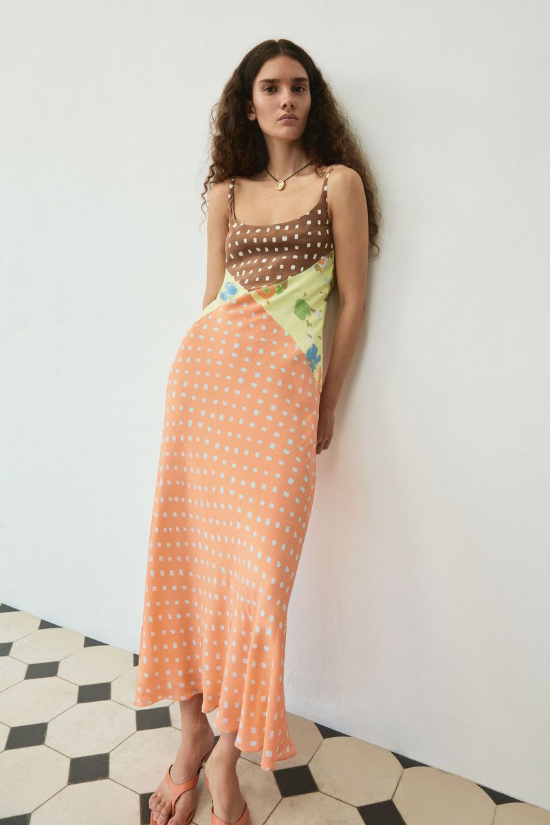 Model in a multi-patterned slip dress leaning against a white wall with patterned tiled flooring