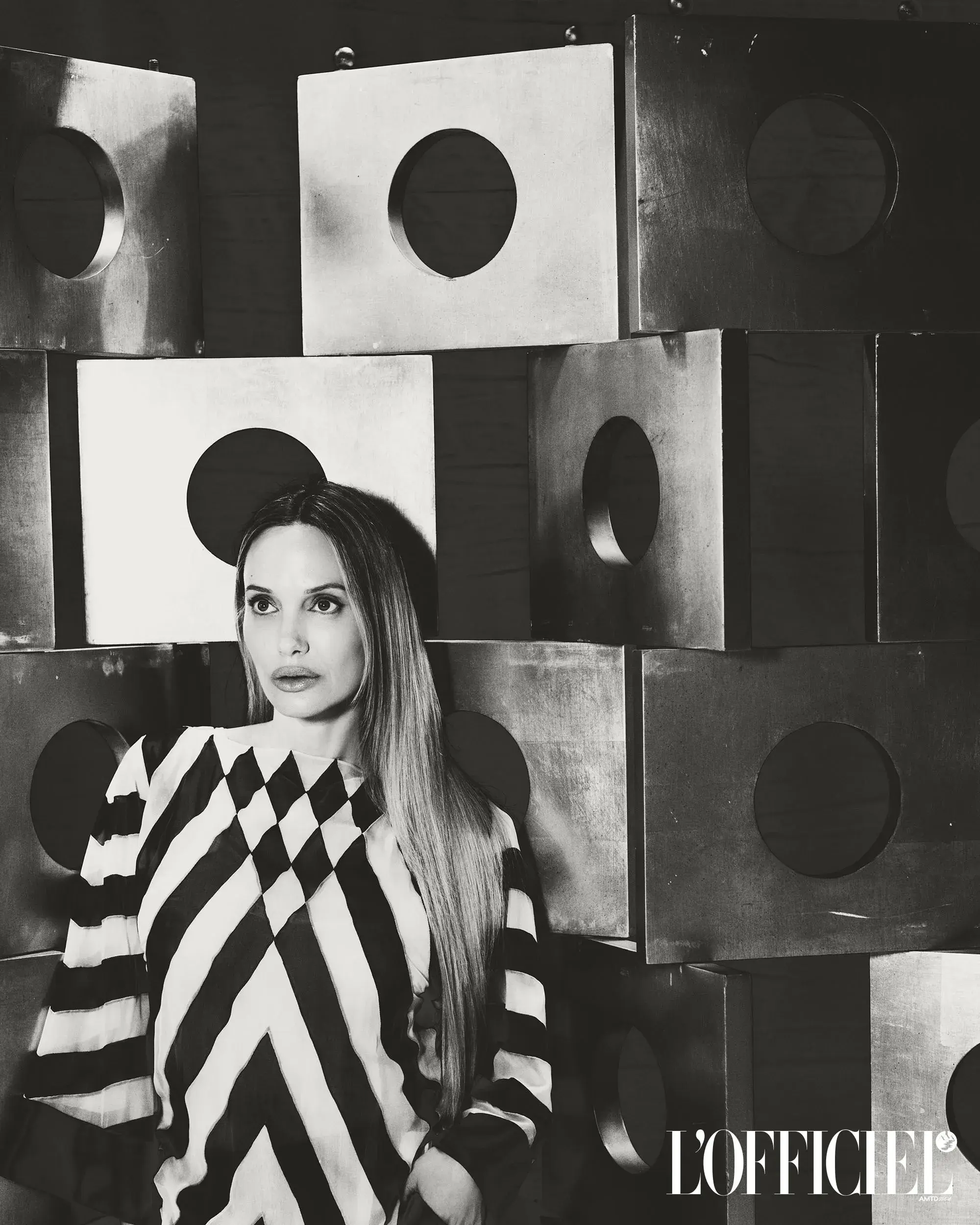 Black and white portrait of Angelina Jolie wearing a striped top against a geometric background for L'Officiel Italia.