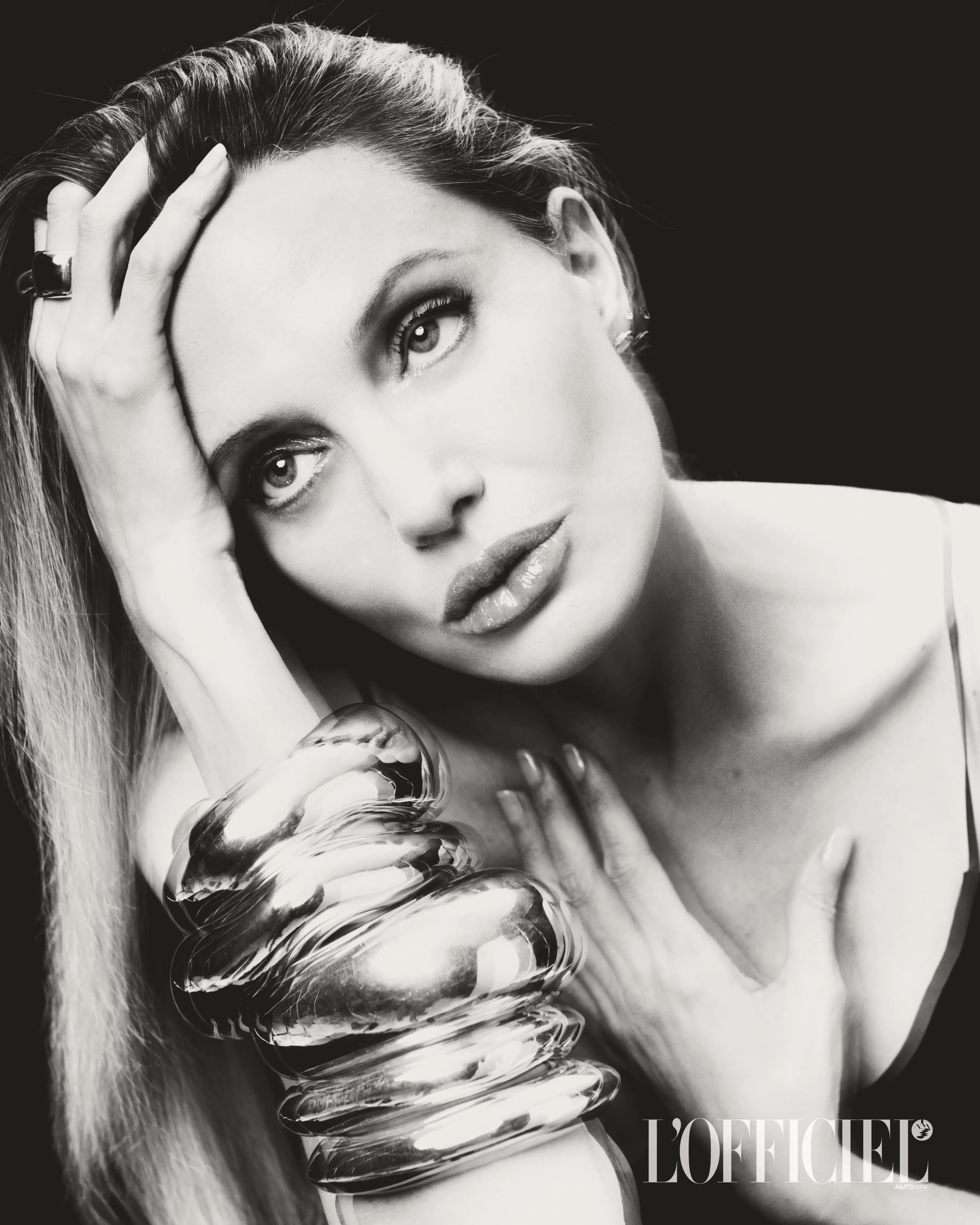 Monochrome portrait of Angelina Jolie wearing heavy silver bangles against a dark background for L'Officiel Italia.