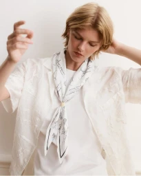 Model wearing a white shirt and printed silk scarf against a plain neutral background for Maison Kitsuné