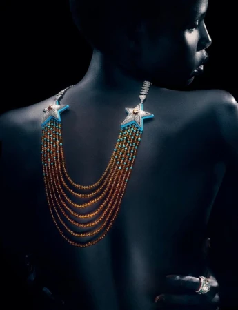 Model Naomi Apajok wearing an elaborate star-motif multi-strand beaded necklace against a dark background