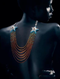 Model Naomi Apajok wearing an elaborate star-motif multi-strand beaded necklace against a dark background
