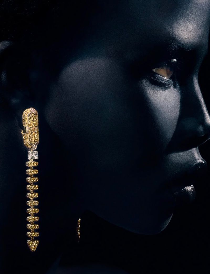Close-up portrait of Naomi Apajok wearing an elaborate gold drop earring under low-key lighting for 10 Magazine Australia