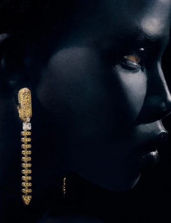 Close-up portrait of Naomi Apajok wearing an elaborate gold drop earring under low-key lighting for 10 Magazine Australia