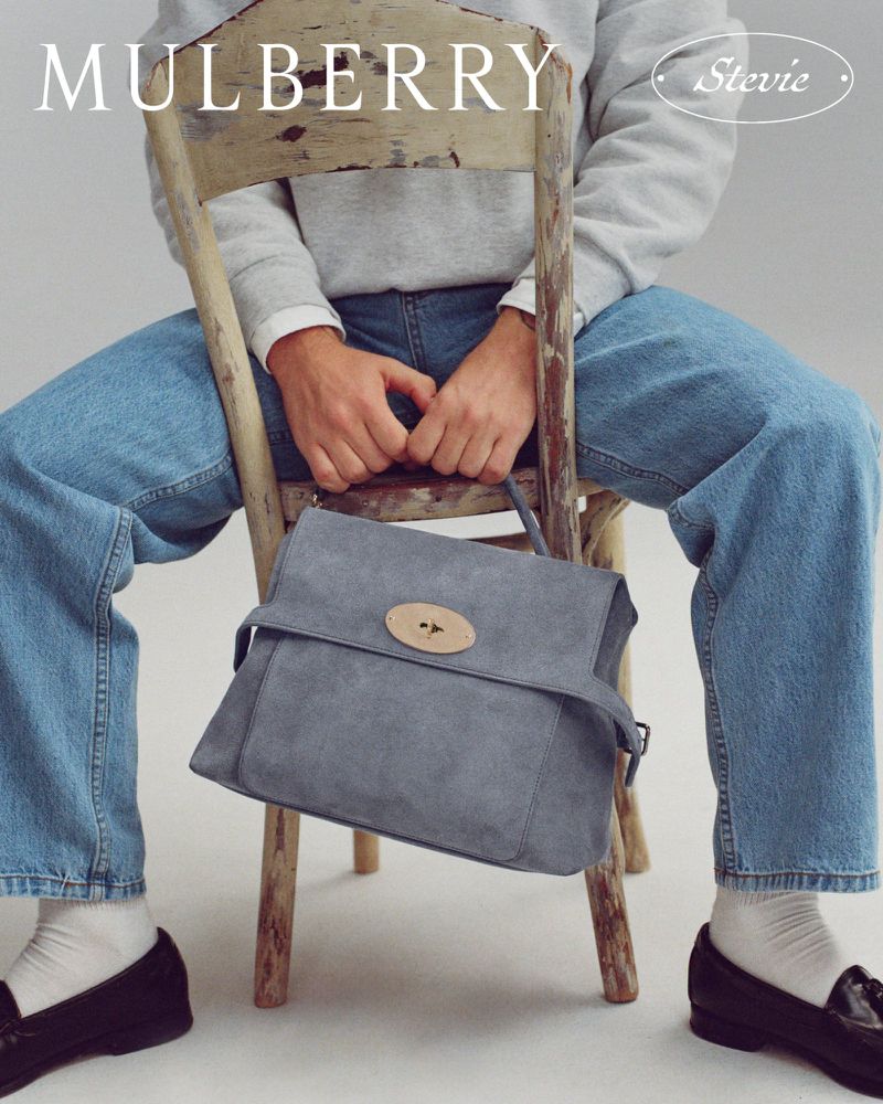 Model sitting on a distressed wooden chair holding a grey leather handbag for Mulberry
