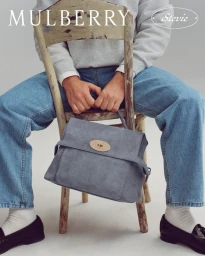 Model sitting on a distressed wooden chair holding a grey leather handbag for Mulberry