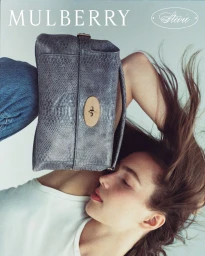 Model holding a grey snakeskin leather Mulberry handbag against a neutral background with hair flowing upwards
