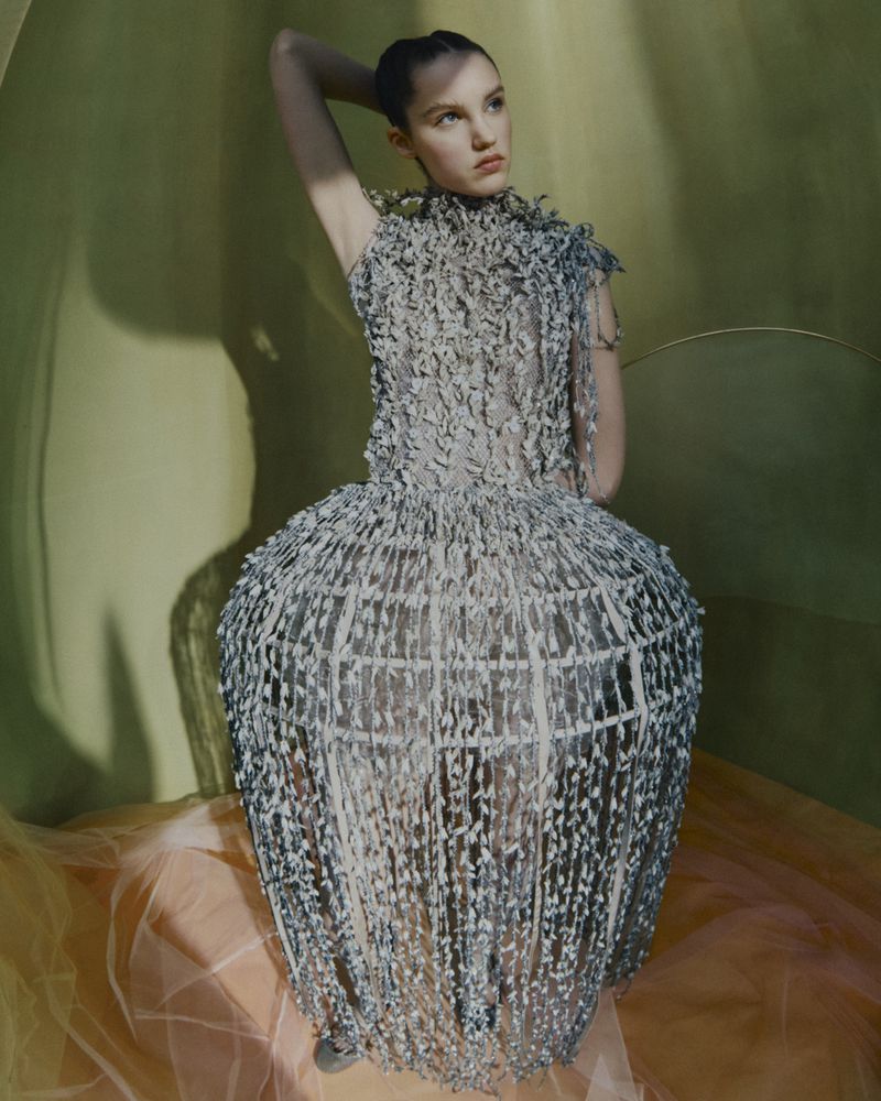 Fashion shot of a woman posing in a sculptural dress, studio lighting against a gradient background.