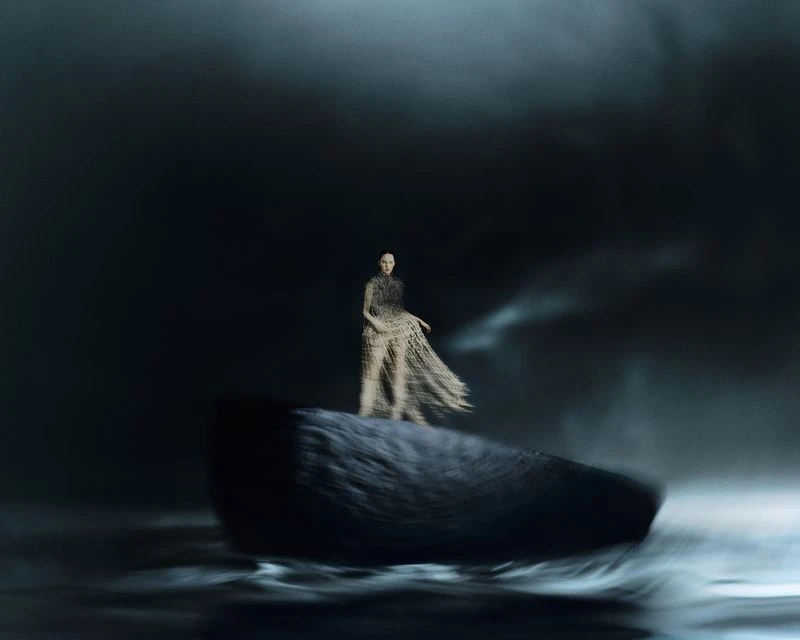 Woman in an airy dress stands on a rocky formation in a dark, atmospheric setting with motion blur, creating a dramatic visual effect.
