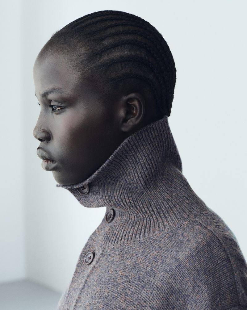 Profile portrait of a model wearing a grey buttoned knit sweater against a plain white studio background.