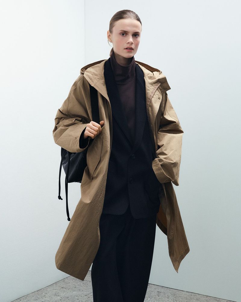Model wearing a brown hooded coat and dark blazer against a plain white studio background.