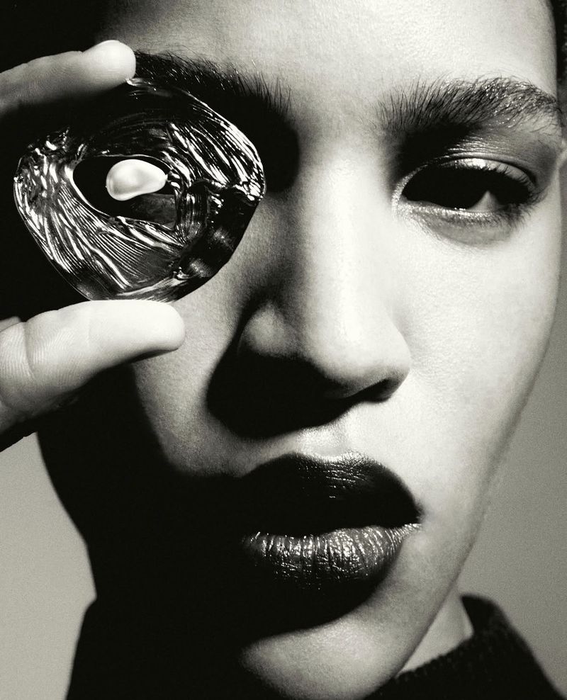 Close-up black and white portrait of a model holding a polished glass object over her eye, captured by Robin Galiegue for Anna Shelley.