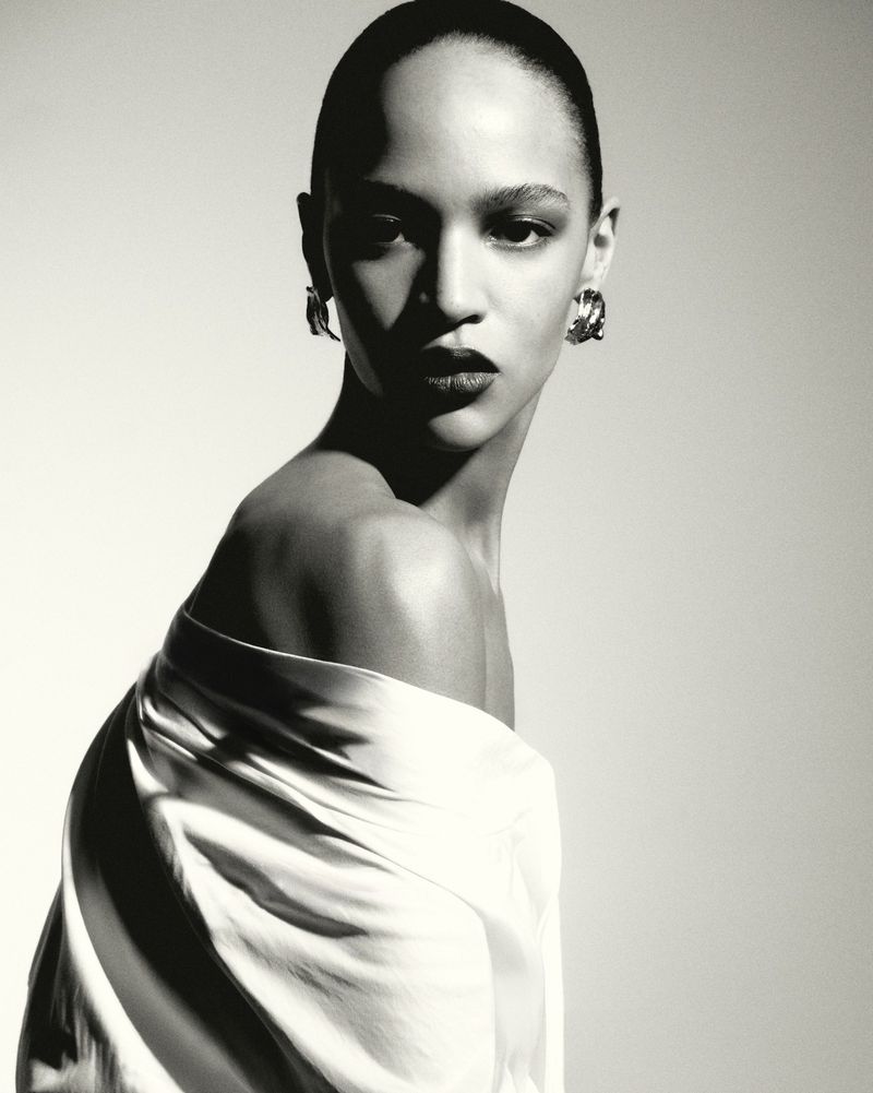 Portrait of a model wearing an off-shoulder white top and silver earrings against a plain background