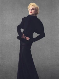Julia Garner in a black high-collar jacket and long skirt against a grey textured studio backdrop for Elle U.S.