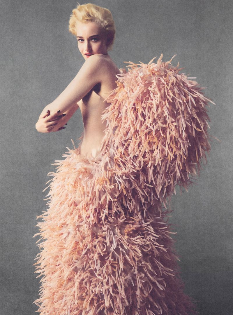 Julia Garner in a voluminous pink feathered garment against a textured grey background for Elle U.S. shot by Allan Hamitouche