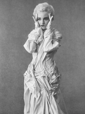 Julia Garner in a long white structured gown with hands to her temples against a textured grey background for Elle U.S.