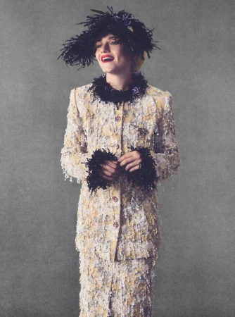 Julia Garner in a textured tweed jacket and feathered hat smiling against a grey textured background for Elle U.S.