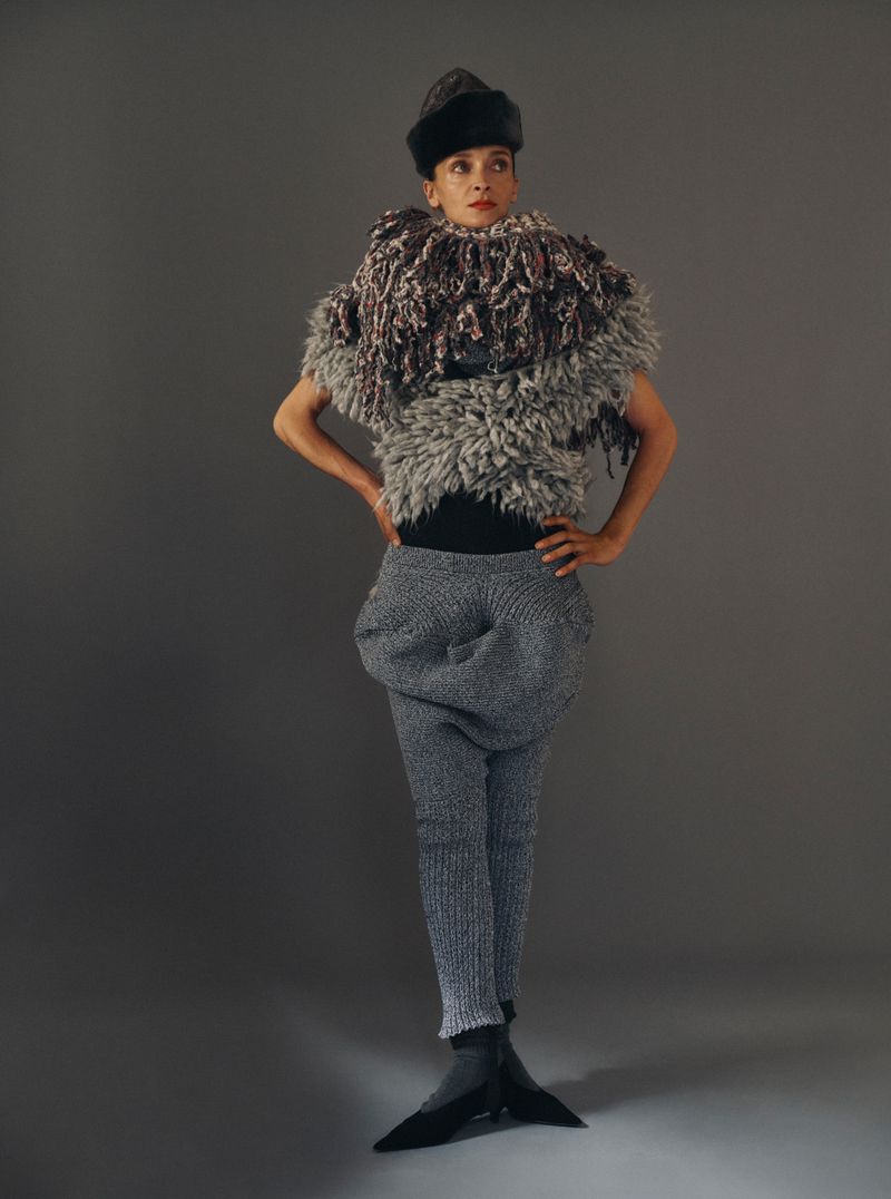Model wearing textured grey knitwear and a dark fur hat against a grey studio backdrop for Mixte.