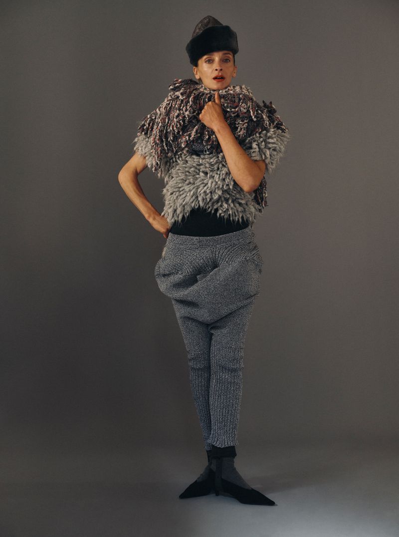 Model wearing textured grey knitwear and a fur cap against a solid grey background