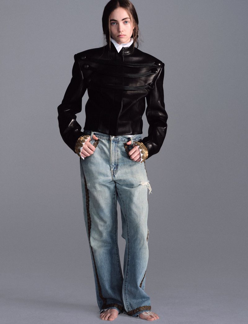 Grace Hartzel in a structured black leather jacket and relaxed blue jeans against a grey studio backdrop.