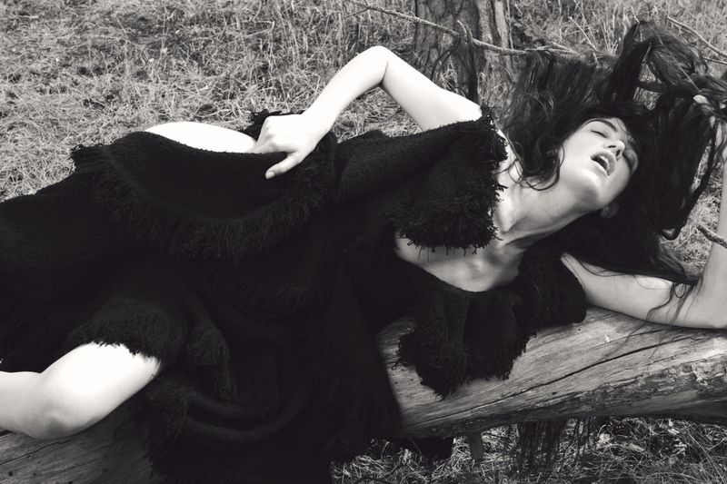 Model Grace Hartzel reclining on a fallen log in a black fringed dress in a woodland setting for Pop Magazine editorial.