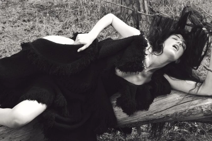 Model Grace Hartzel reclining on a fallen log in a black fringed dress in a woodland setting for Pop Magazine editorial.