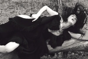 Model Grace Hartzel reclining on a fallen log in a black fringed dress in a woodland setting for Pop Magazine editorial.