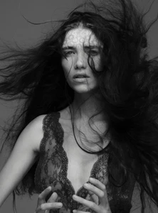 Portrait of model Grace Hartzel with dark flowing hair in a lace dress against a grey studio backdrop for Pop Magazine editorial.