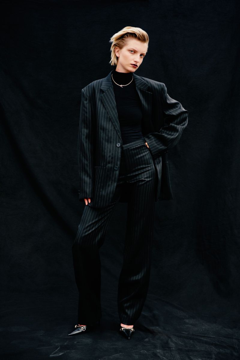 Model wearing a dark pinstripe oversized suit and black turtleneck against a dark textured backdrop for Vogue Czechoslovakia.