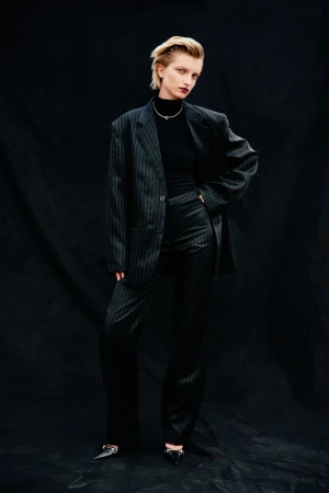 Model wearing a dark pinstripe oversized suit and black turtleneck against a dark textured backdrop for Vogue Czechoslovakia.