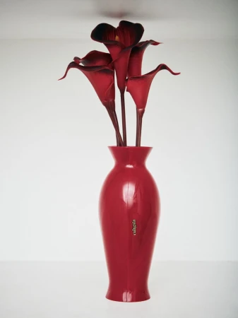 Deep red calla lily flowers arranged in a matching glossy red ceramic vase against a clean white seamless studio background.