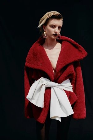 Model wearing a red faux-fur coat with a large white tied sash against a black backdrop for Vogue Czechoslovakia.