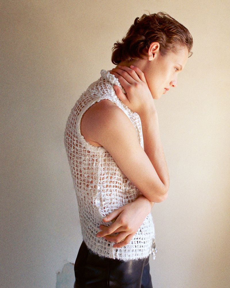 Model in a white knit sleeveless top with hands touching neck against a neutral background for The Gentlewoman editorial Cut Outs.
