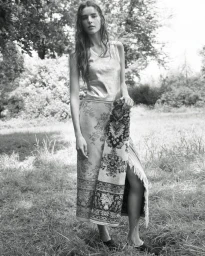 Model standing outdoors in a grassy field wearing a patterned skirt and holding a fringed textile for The Gentlewoman.