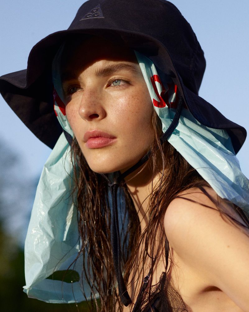 Close-up portrait of a woman wearing a black bucket hat and light blue scarf against a clear sky