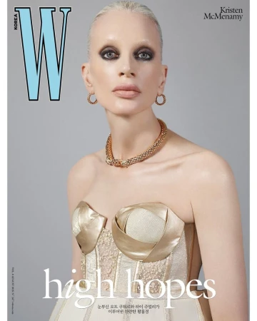Magazine cover of Kristen McMenamy wearing jewelry and a strapless gold and white gown in a studio with a neutral backdrop.