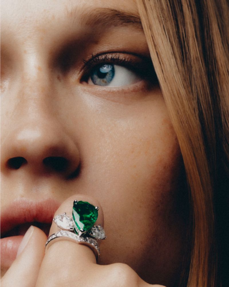 Close-up portrait of a woman wearing a large green gemstone ring near her lips