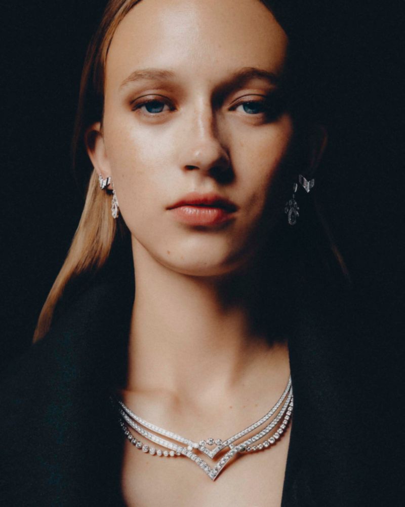 Close-up portrait of a female model wearing diamond earrings and a layered diamond necklace against a dark background