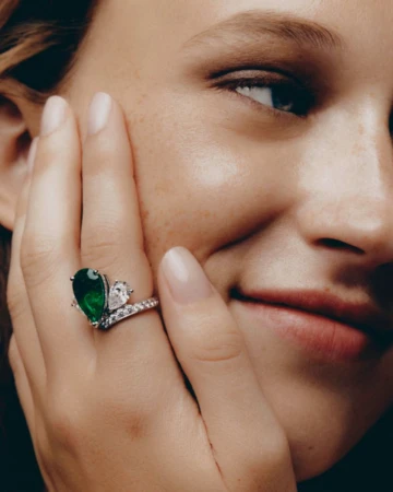 Close-up portrait of a woman wearing an emerald ring with diamonds on her hand against her cheek