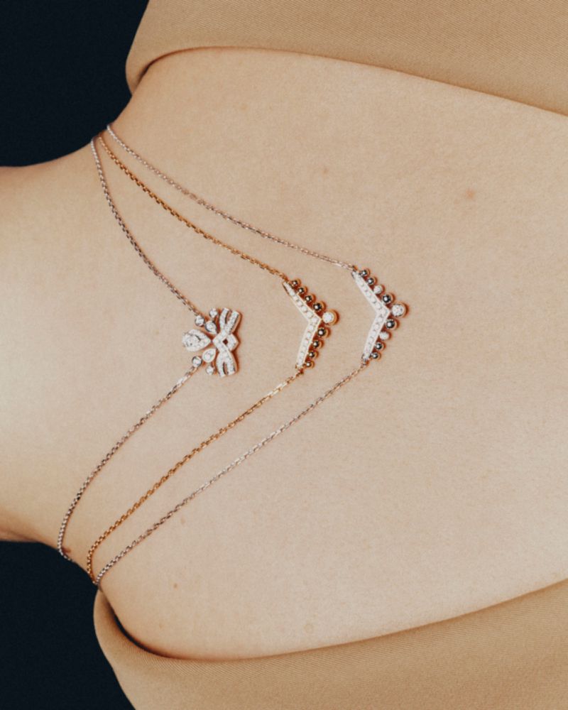 Close-up portrait featuring three delicate diamond and gold necklaces draped gracefully across bare back.