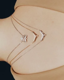 Close-up portrait featuring three delicate diamond and gold necklaces draped gracefully across bare back.